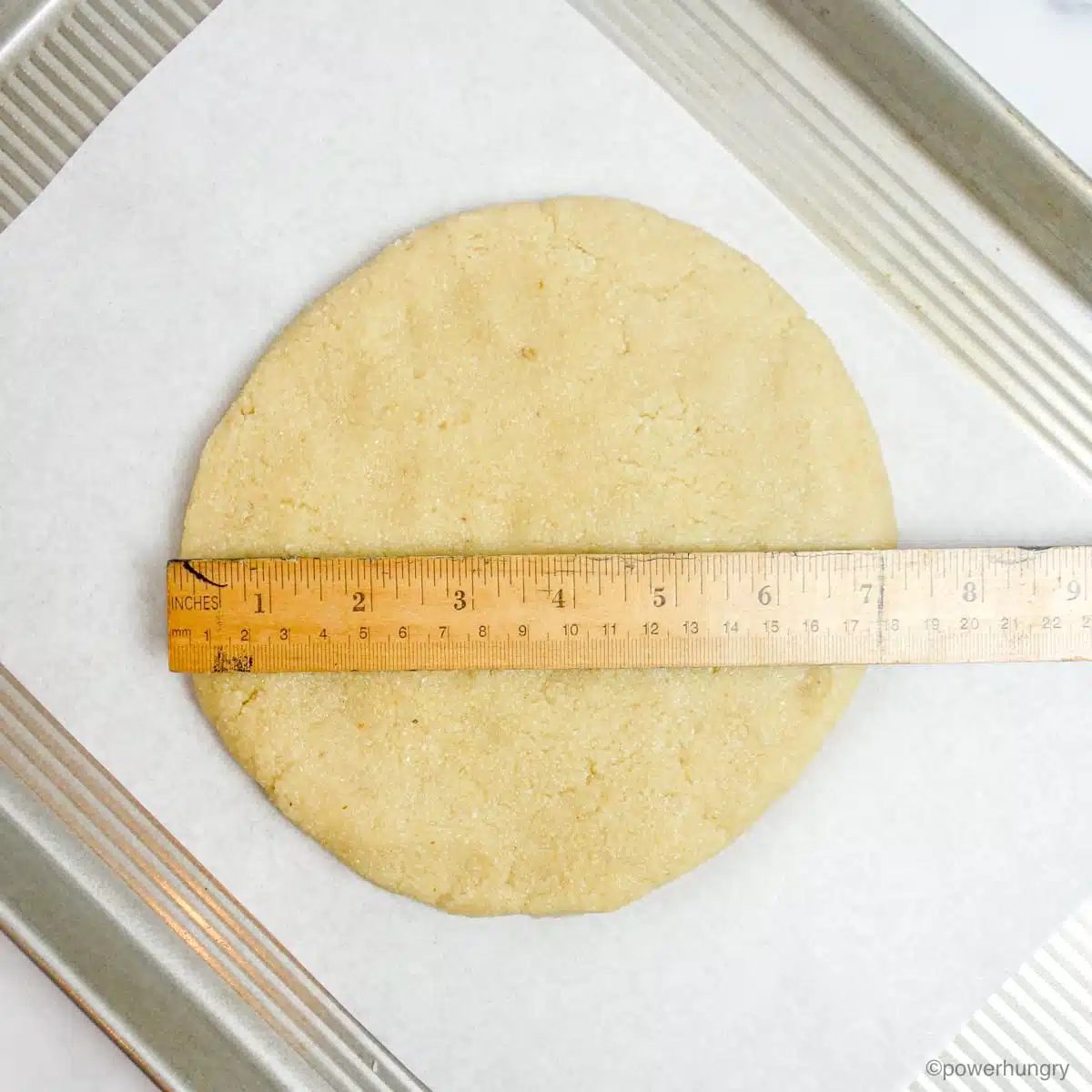 almond flour dough disk on a baking sheet with a ruler on top