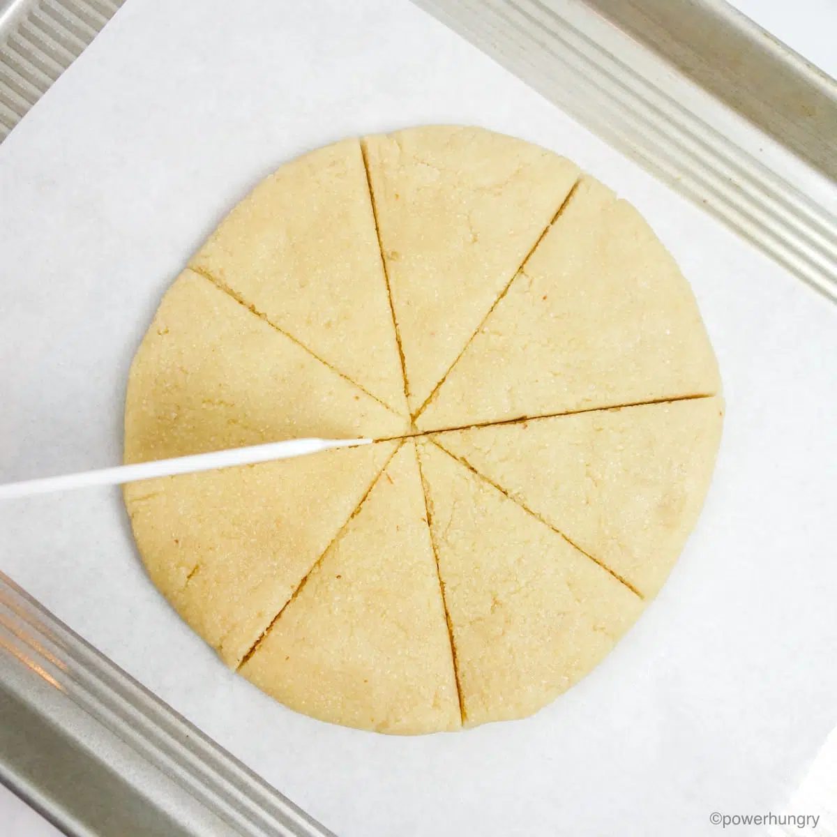almond flour scone dough disk on a baking sheet, being cut into 8 wedges