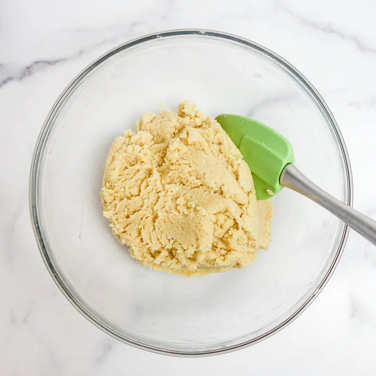 a glass bowl filled with almond flour scone dough, a green spatula alongside