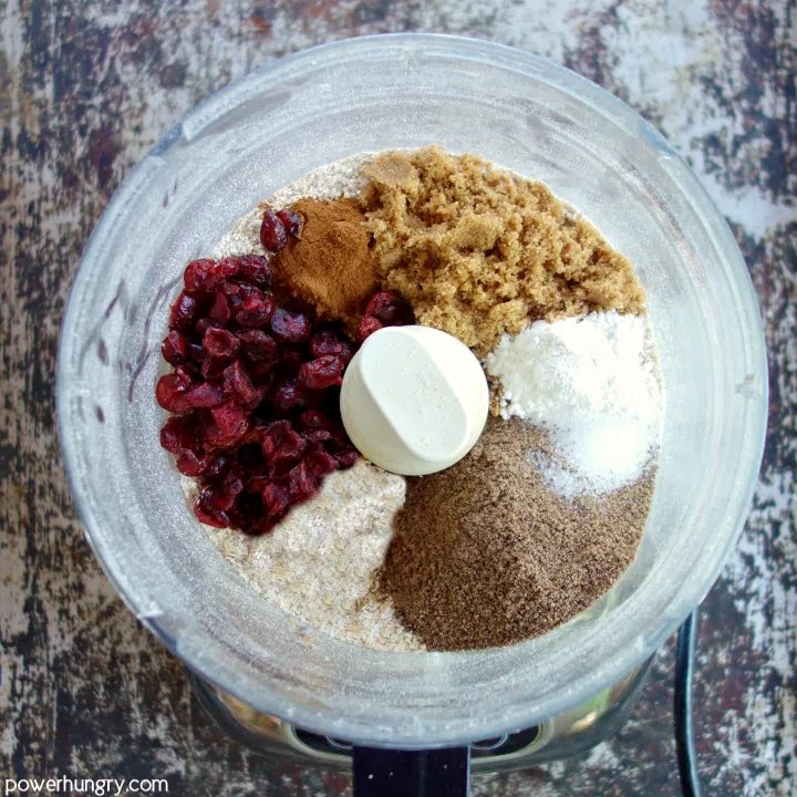 food processor with chopped rolled oats, dried cranberries, flax, coconut sugar, and cinnamon
