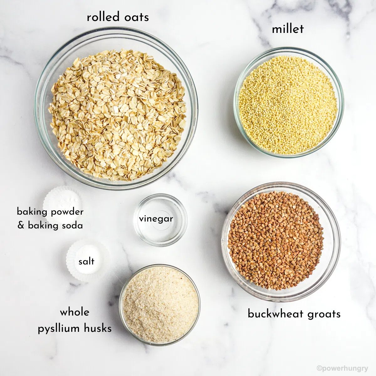 ingredients for multigrain sandwich bread, all in glass bowls on a marble countertop