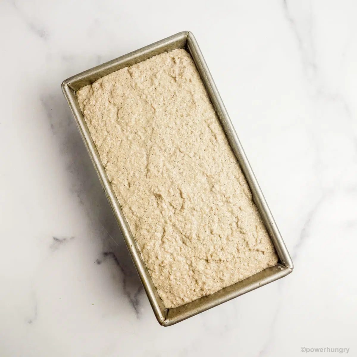 multigrain batter in a prepare baking tin atop a marble countertop