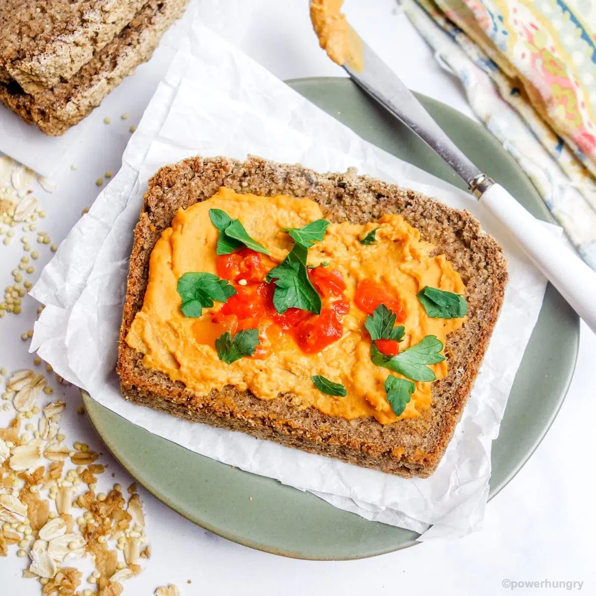 a slice of multigrain bread on an olive-colored plate, topped with hummus