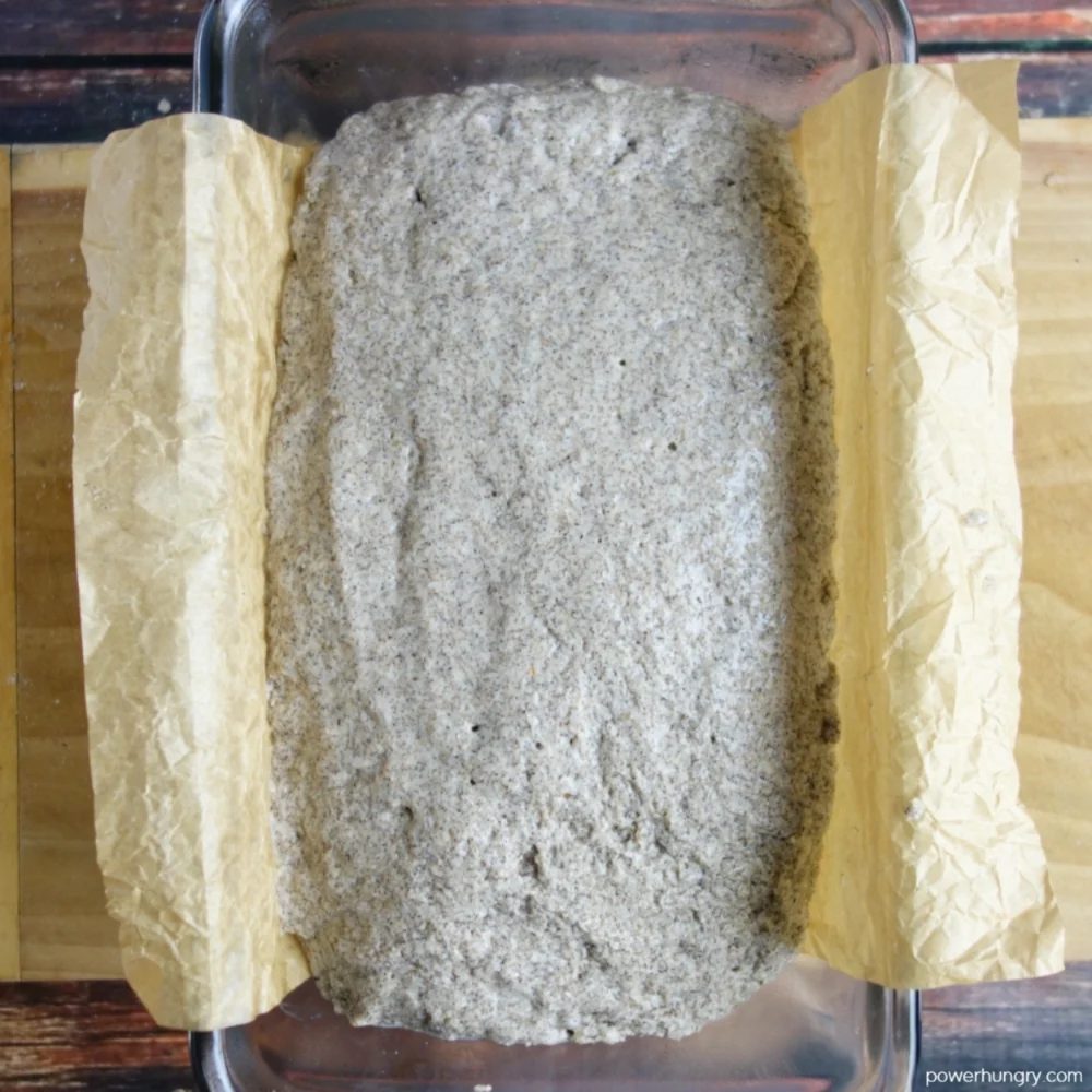 buckwheat bread dough in a parchment paper lined glass loaf baking pan