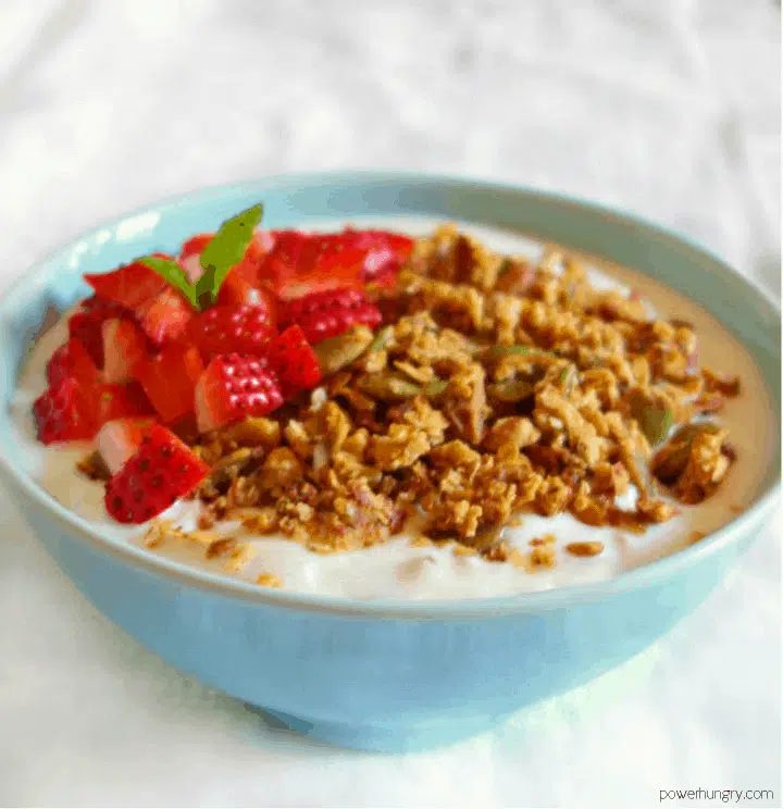 grain-free banana granola in a light blue bowl with strawberries and nondairy milk