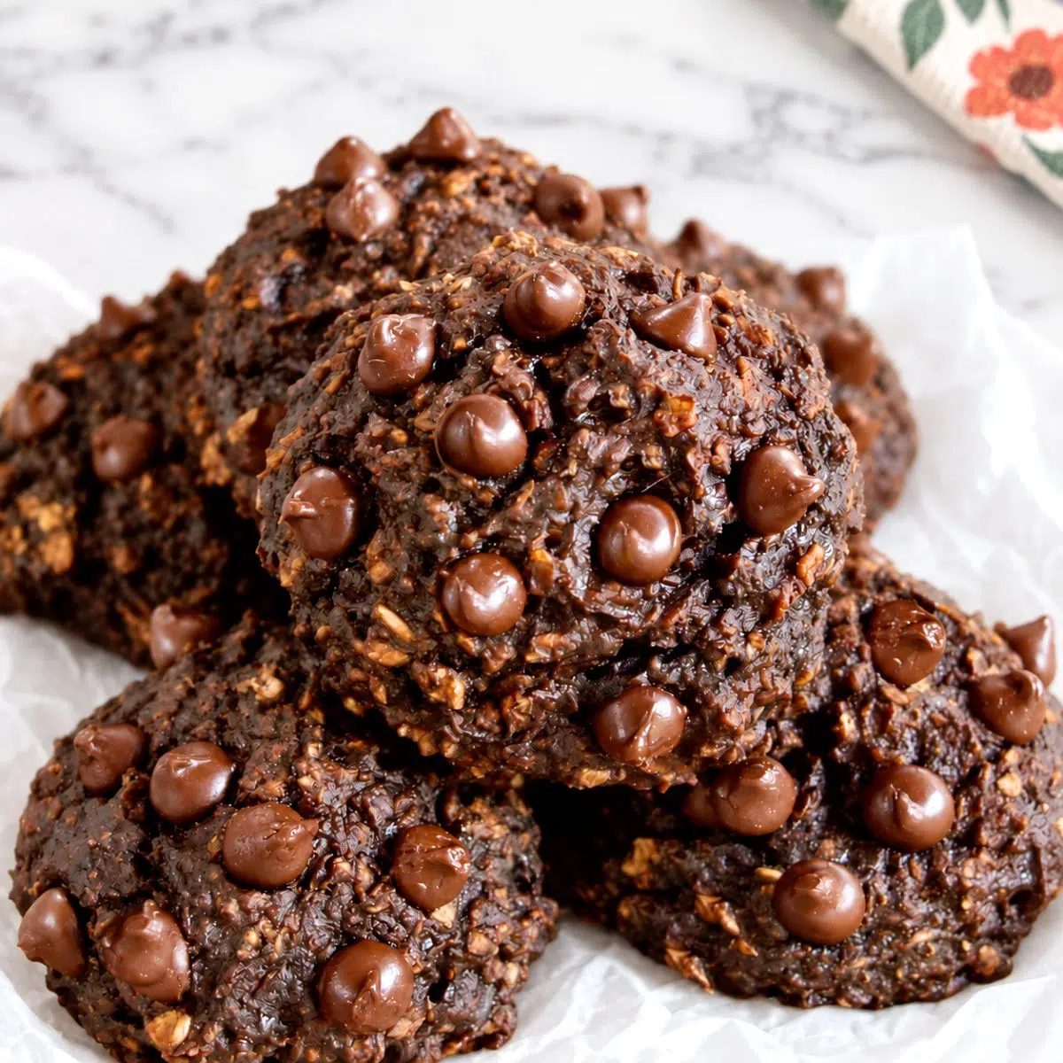 a pile of chocolate oat banana cookies on white parchment paper