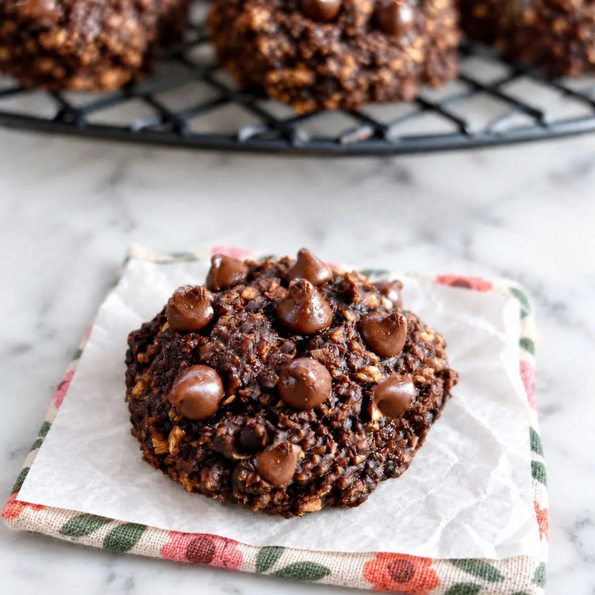 a single chocolate banana oat cookie with more behind on a cooling rack