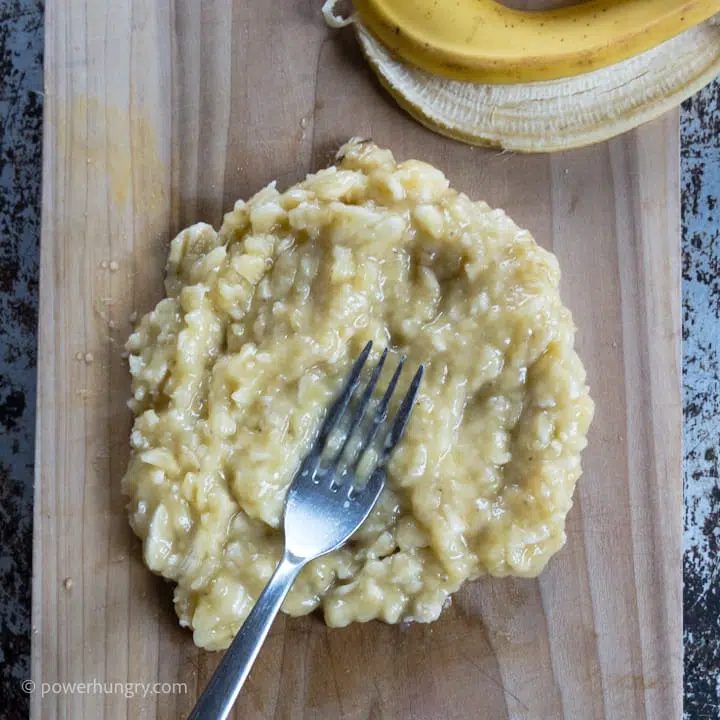 mashed very ripe banana with a fork on a wooden cutting board.