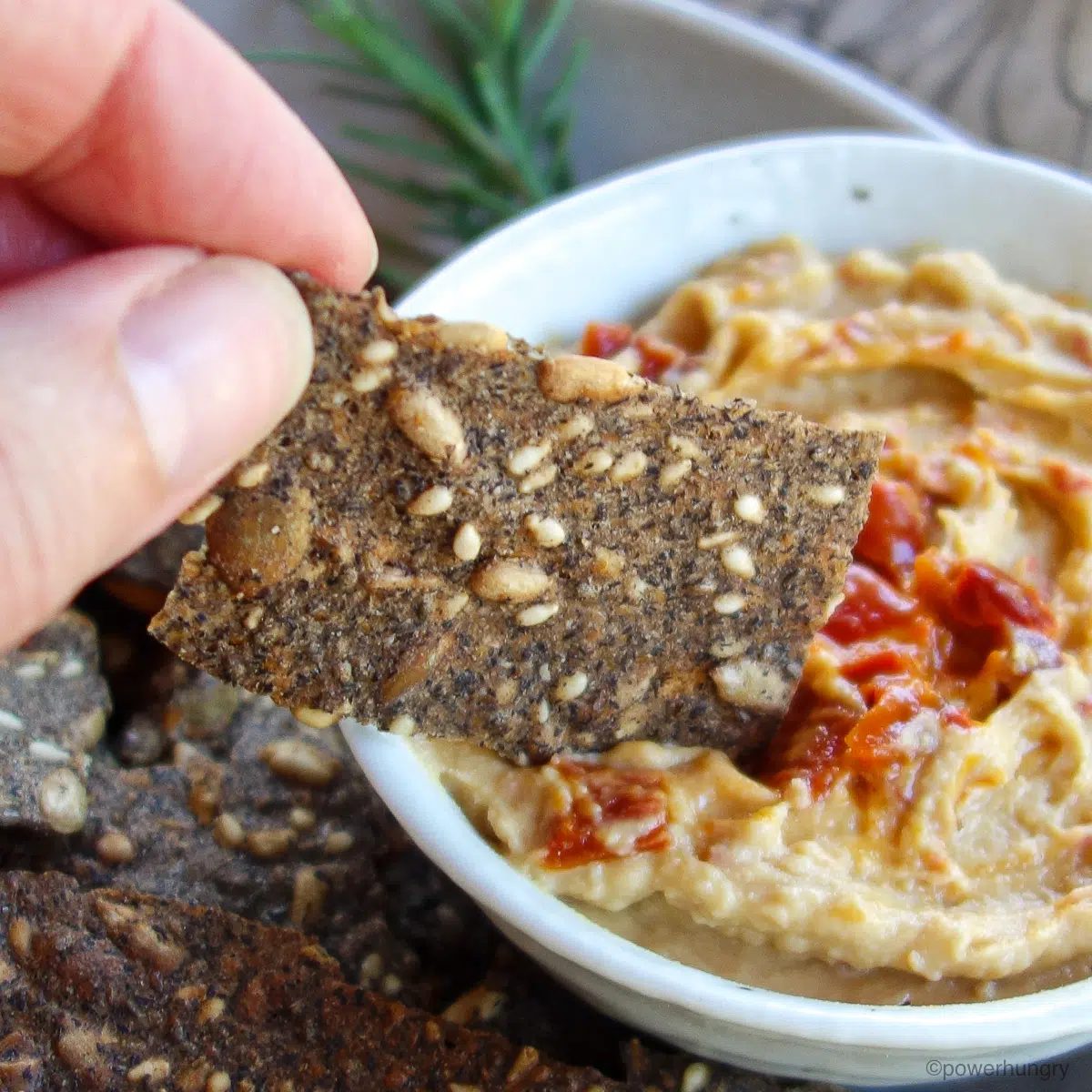 buckwheat cracker getting dipped into white bowl filled with hummus