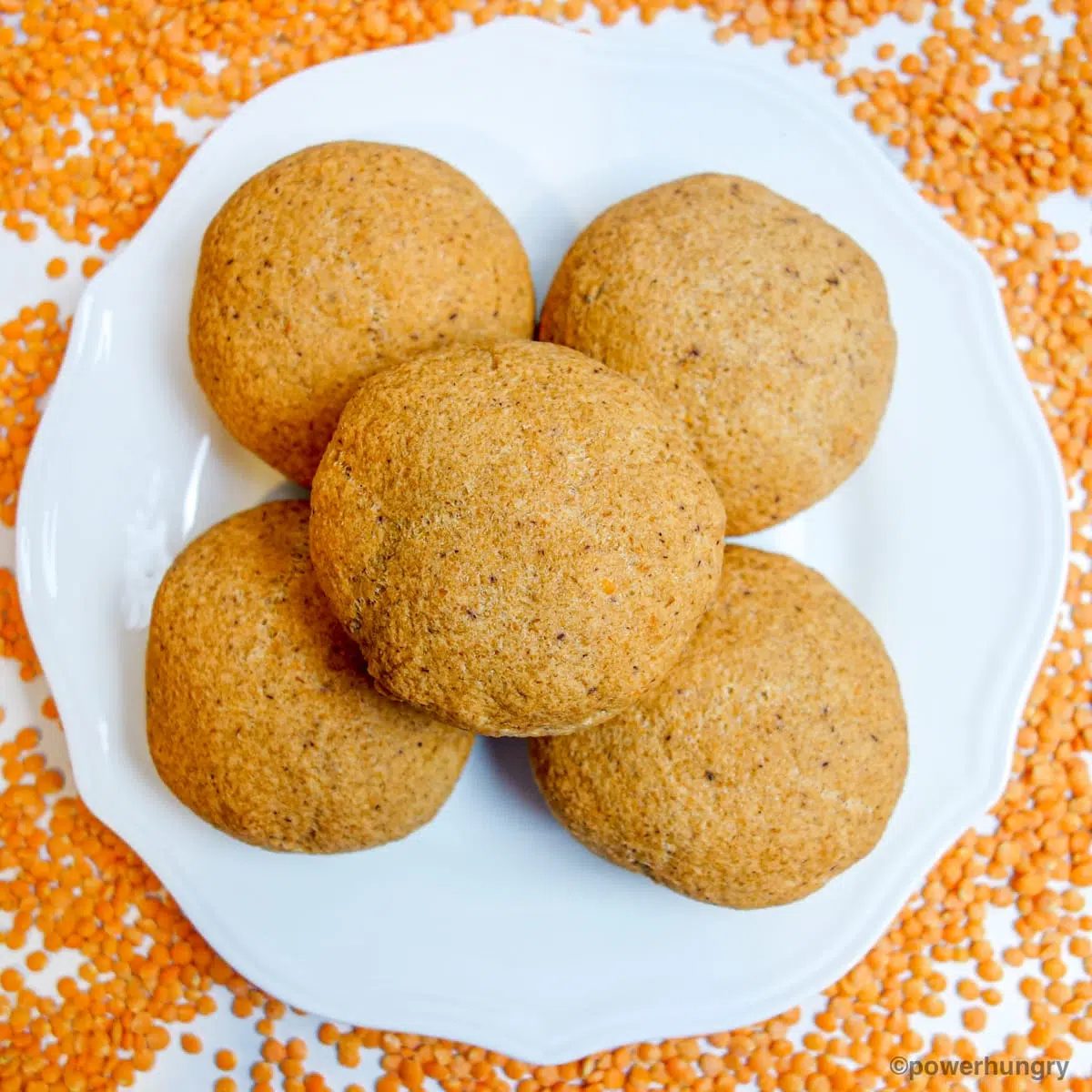 a white plate with lentil bread rolls , surrounded by red lentils
