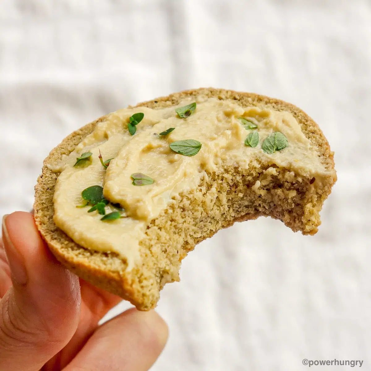 half of a piece of gluten-free lentil bread topped with hummus and fresh herbs