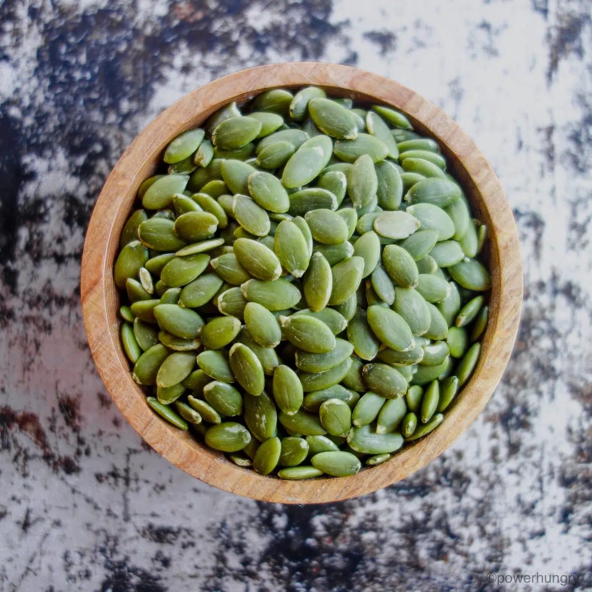 overhead photo of a wooden bowl filled with raw green pumpkin seeds (pepitas)