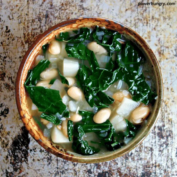 overhead shot of Kale Potato & White Bean Soup in a pottery bowl