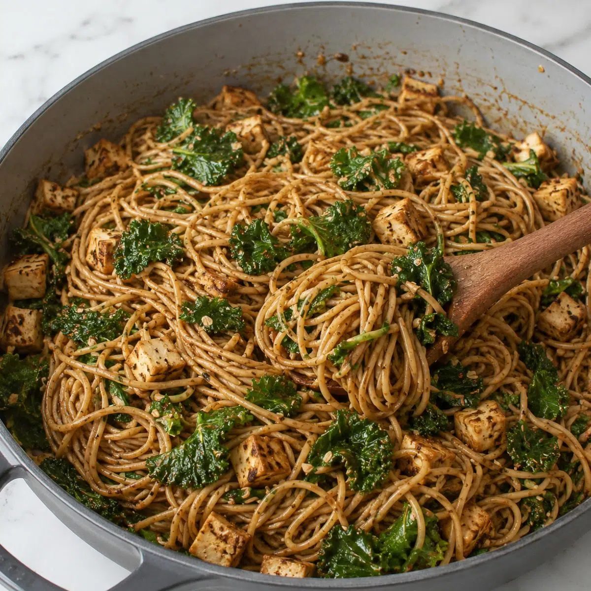 grey enamel cast iron skillet filled with kale tofu soba noodles stir-fry