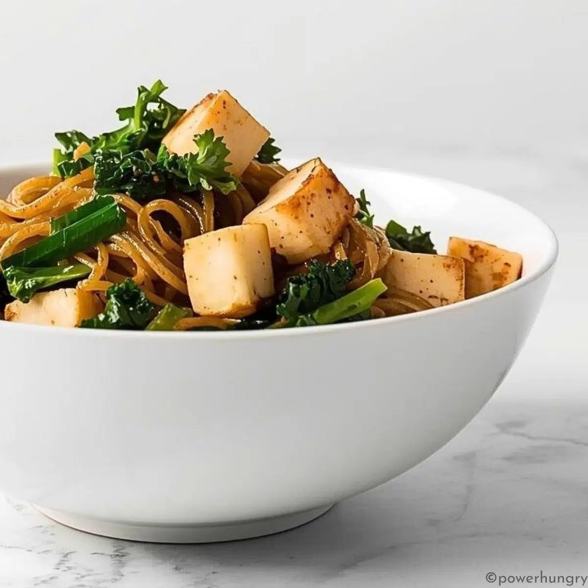 close up of a white bowl filled with kale tofu soba noodles