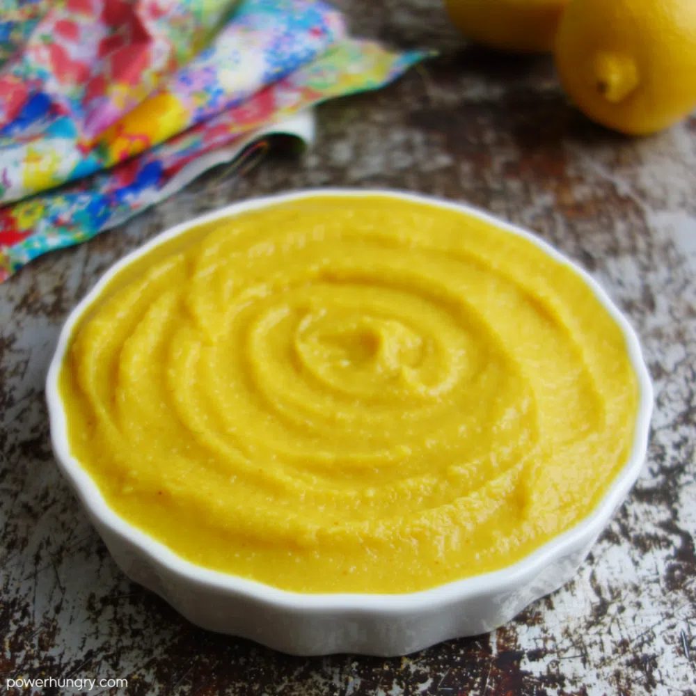 white bowl filled with split pea hummus, with a colorful napkin and lemons in the background