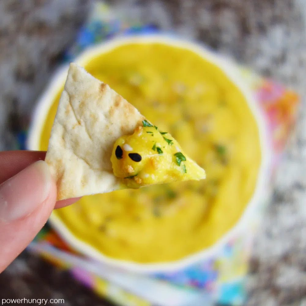 close up of a pita chip topped with split pea favasalata (pea hummus)