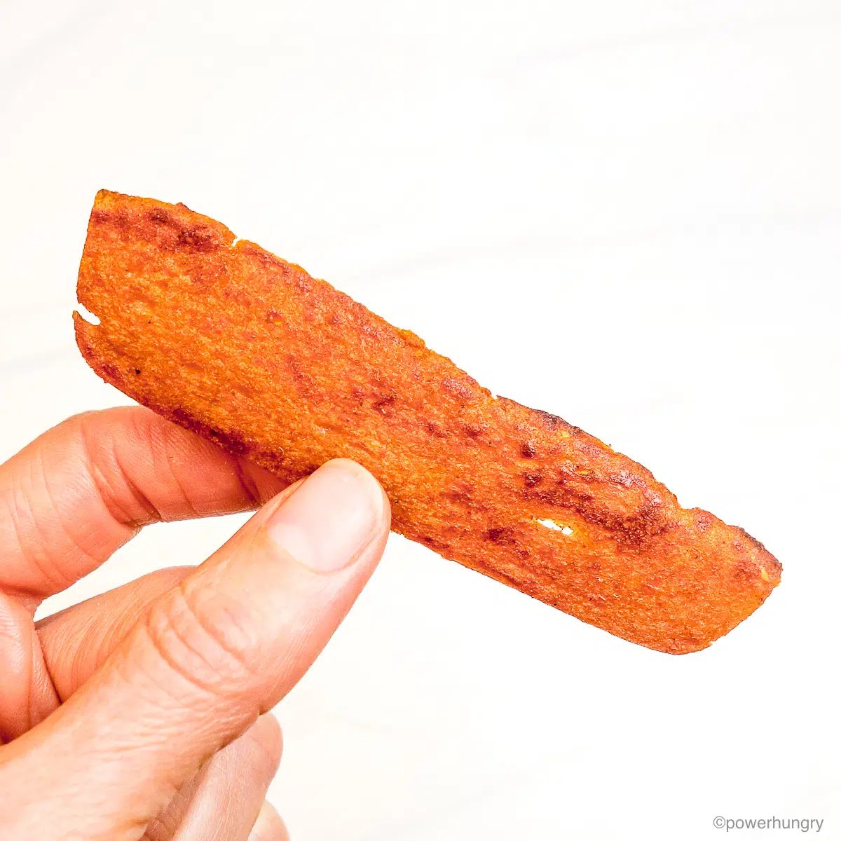 a single strip of lentil bacon, held in a hand