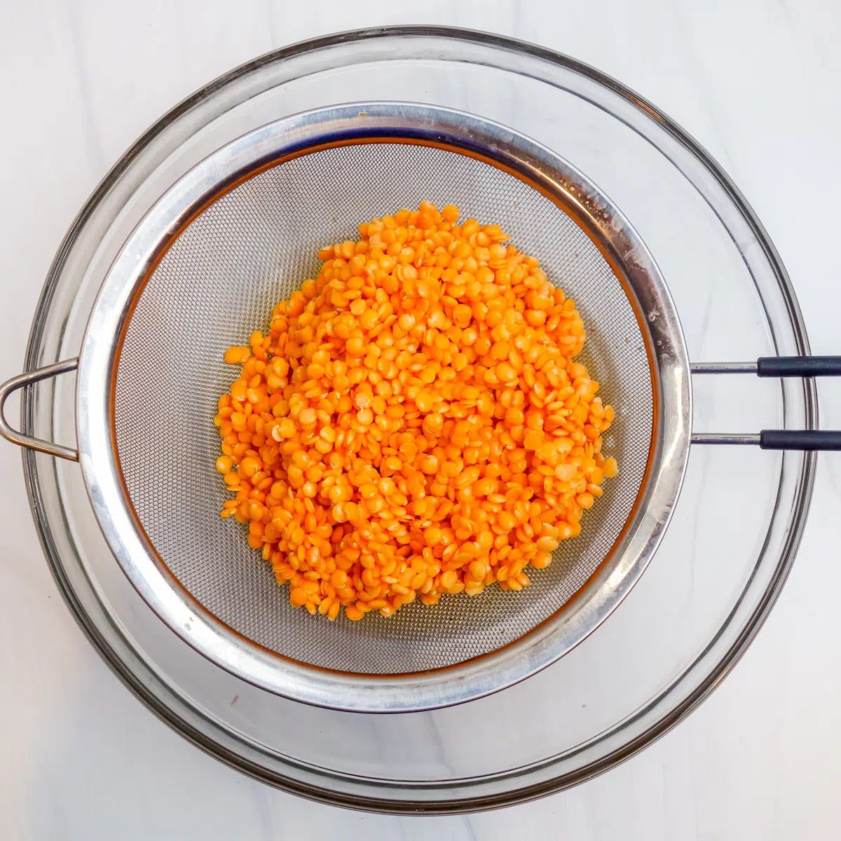 soaked red lentils being drained in a mesh strainer