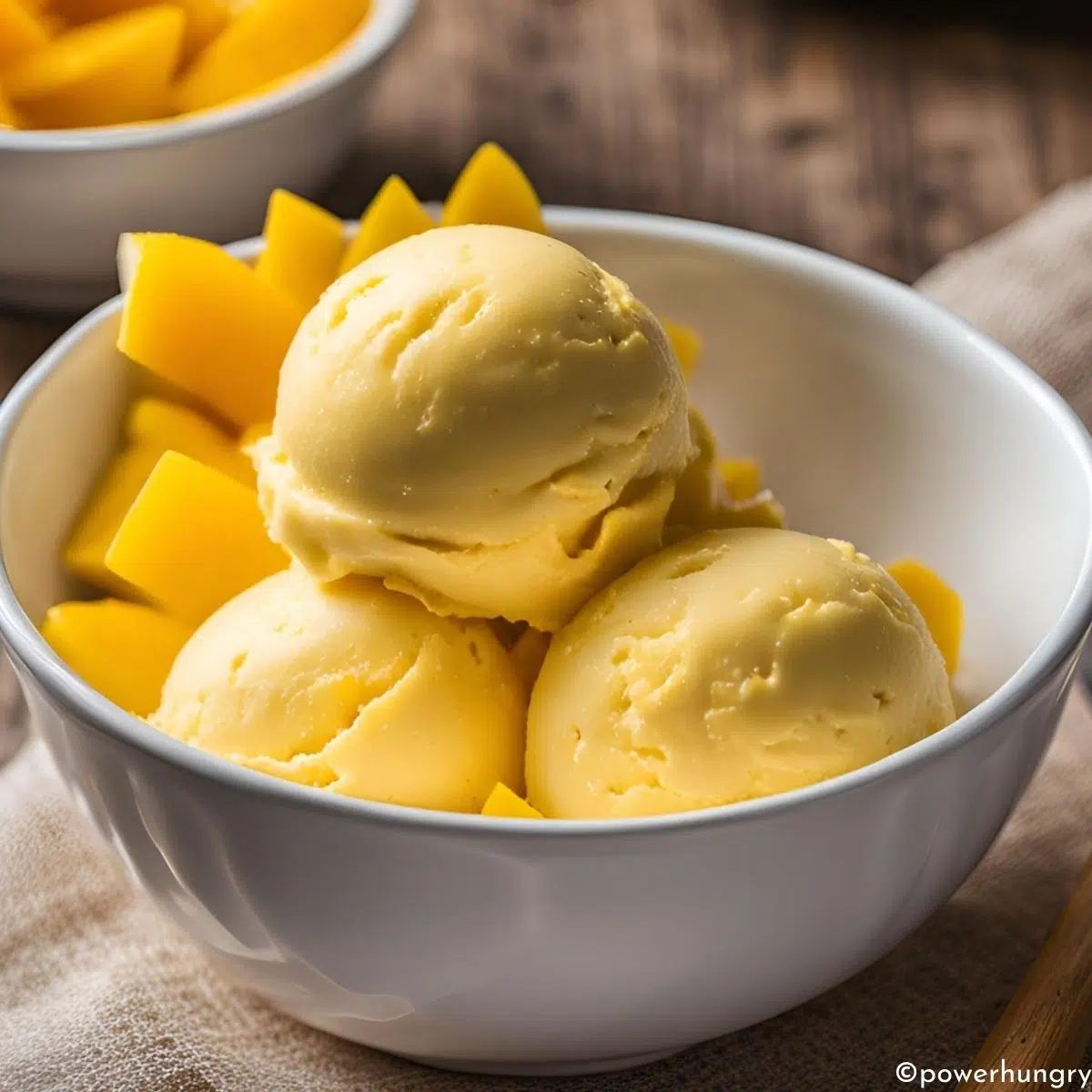 mango ice cream in a white bowl with diced mango included