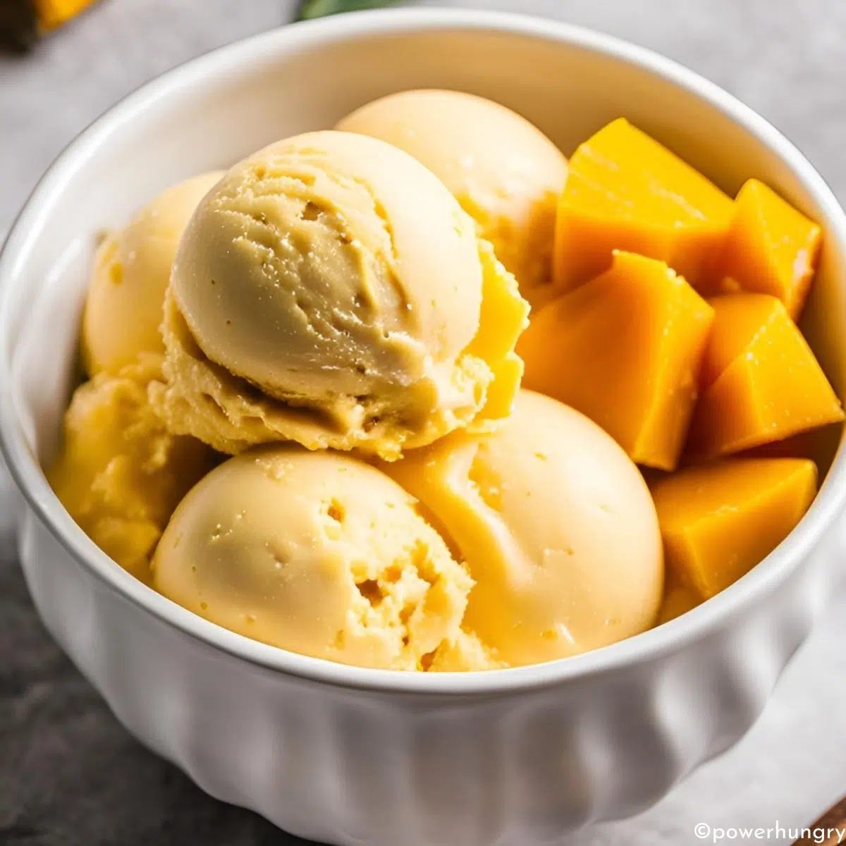 mango ice cream in a white bowl with some diced mango in the bowl