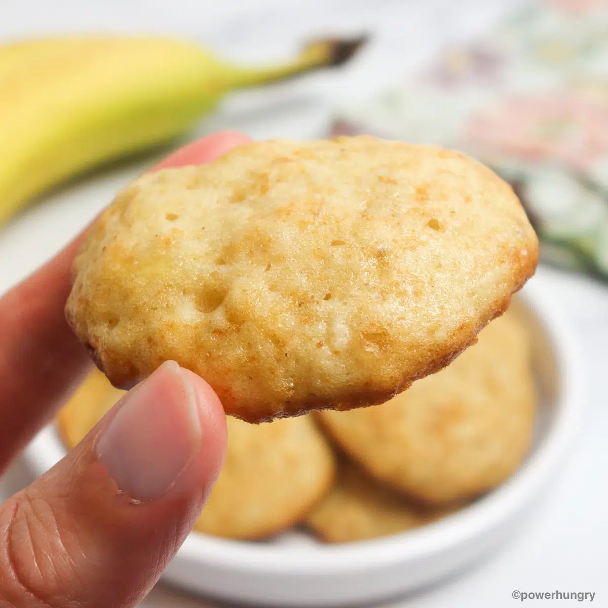 a single banana millet flour cookie held in fingertips