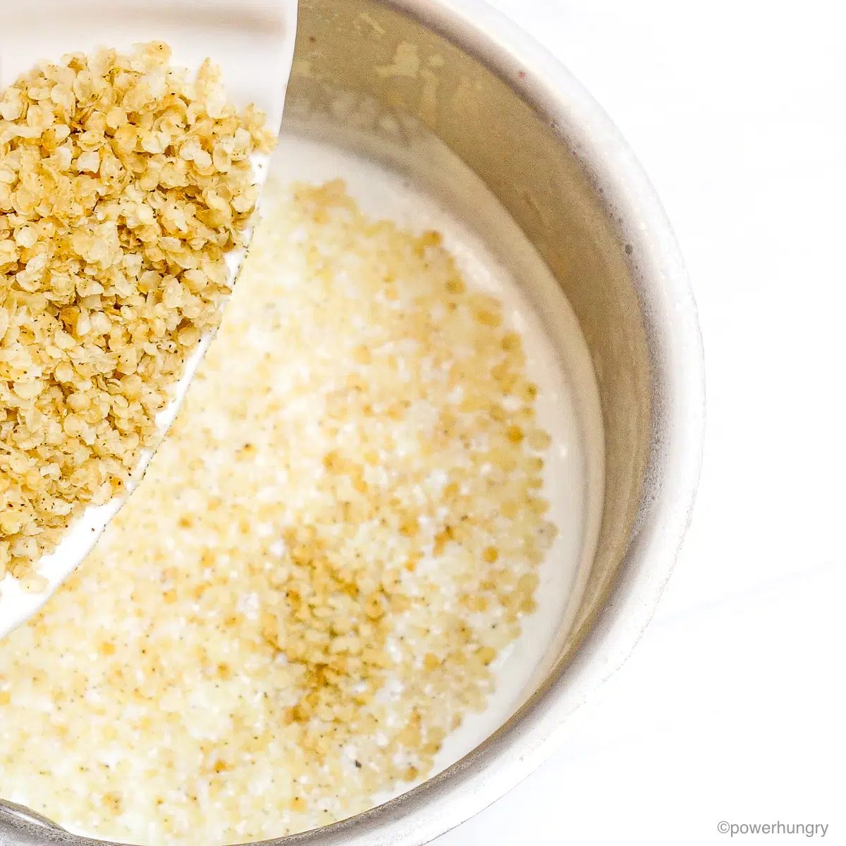 millet flakes getting added to the milk mixture in a saucepan.