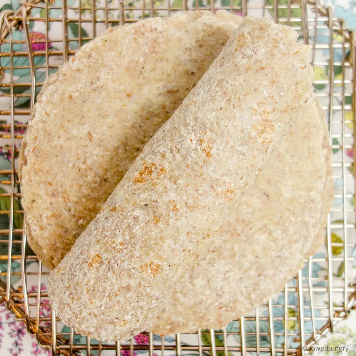 overhead shot of millet tortillas on a cooling rack, with the top tortilla rolled up
