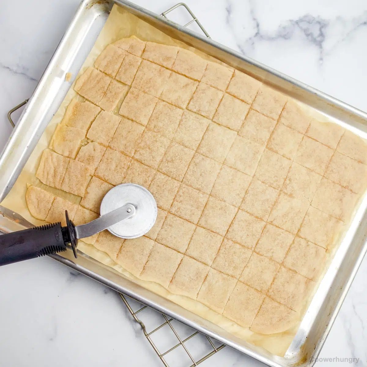 cassava flour crackers on a baking sheet being cut with a pizza cutter