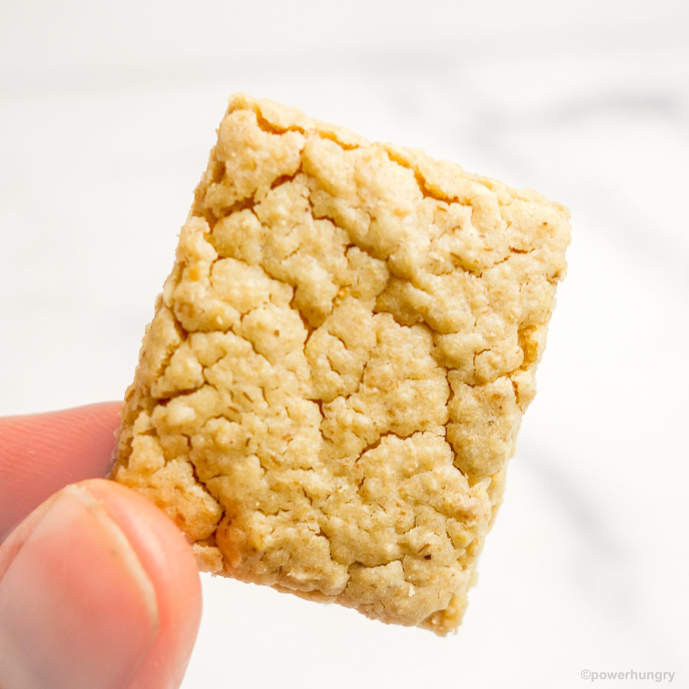 a single vegan oat cracker held in someone's fingertips