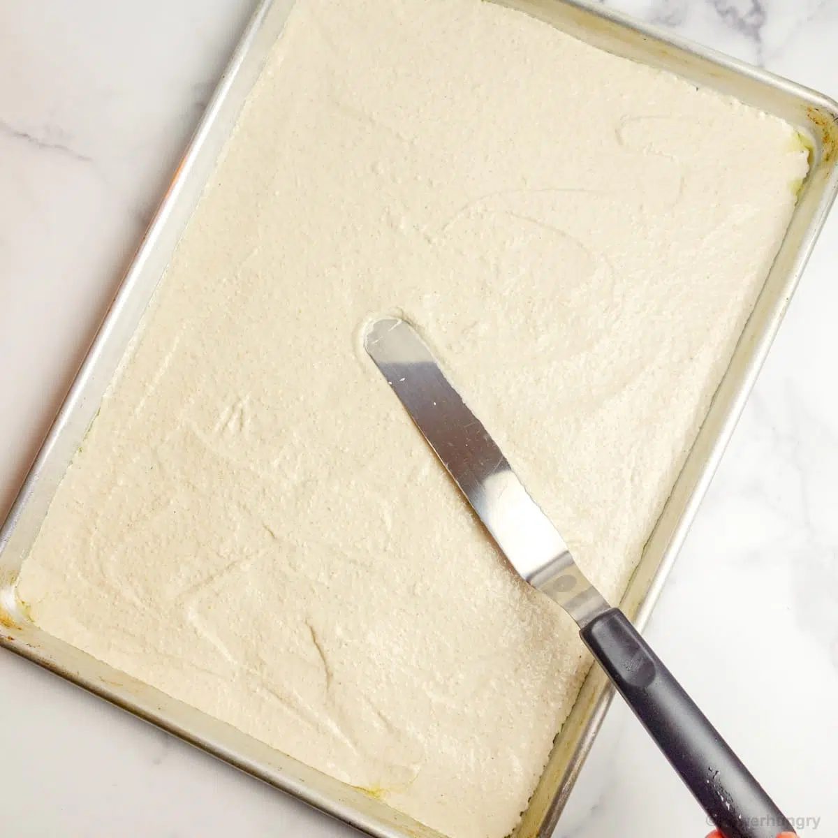 offset spatula spreading cracker batter onto a half baking sheet