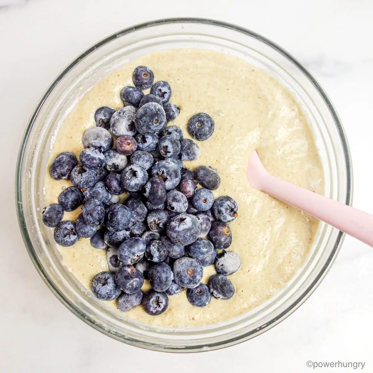 clear glass bowl full of oil-free vegan oat blueberry muffins batter and topped with blueberries
