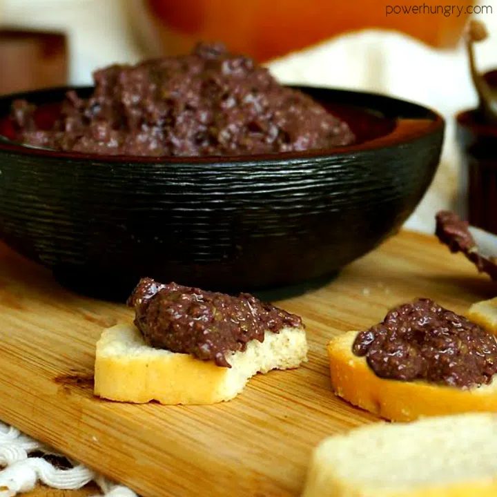 close up of a side view of olive tapenade with toasts, spread with the tapenade, in the foreground