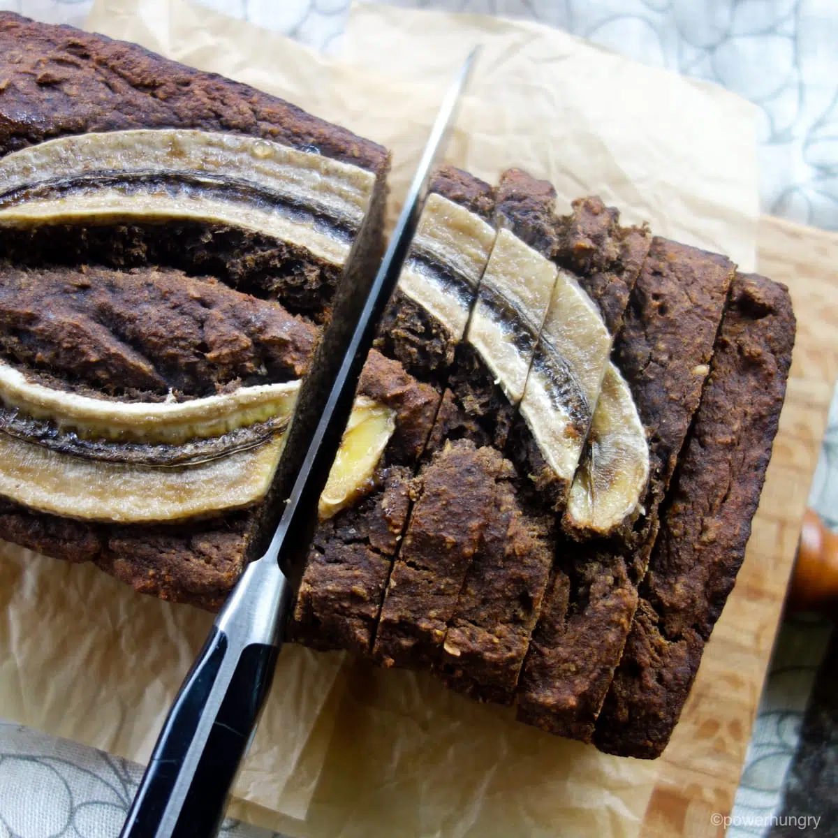 buckwheat banana bread on a wooden cutting board, getting sliced
