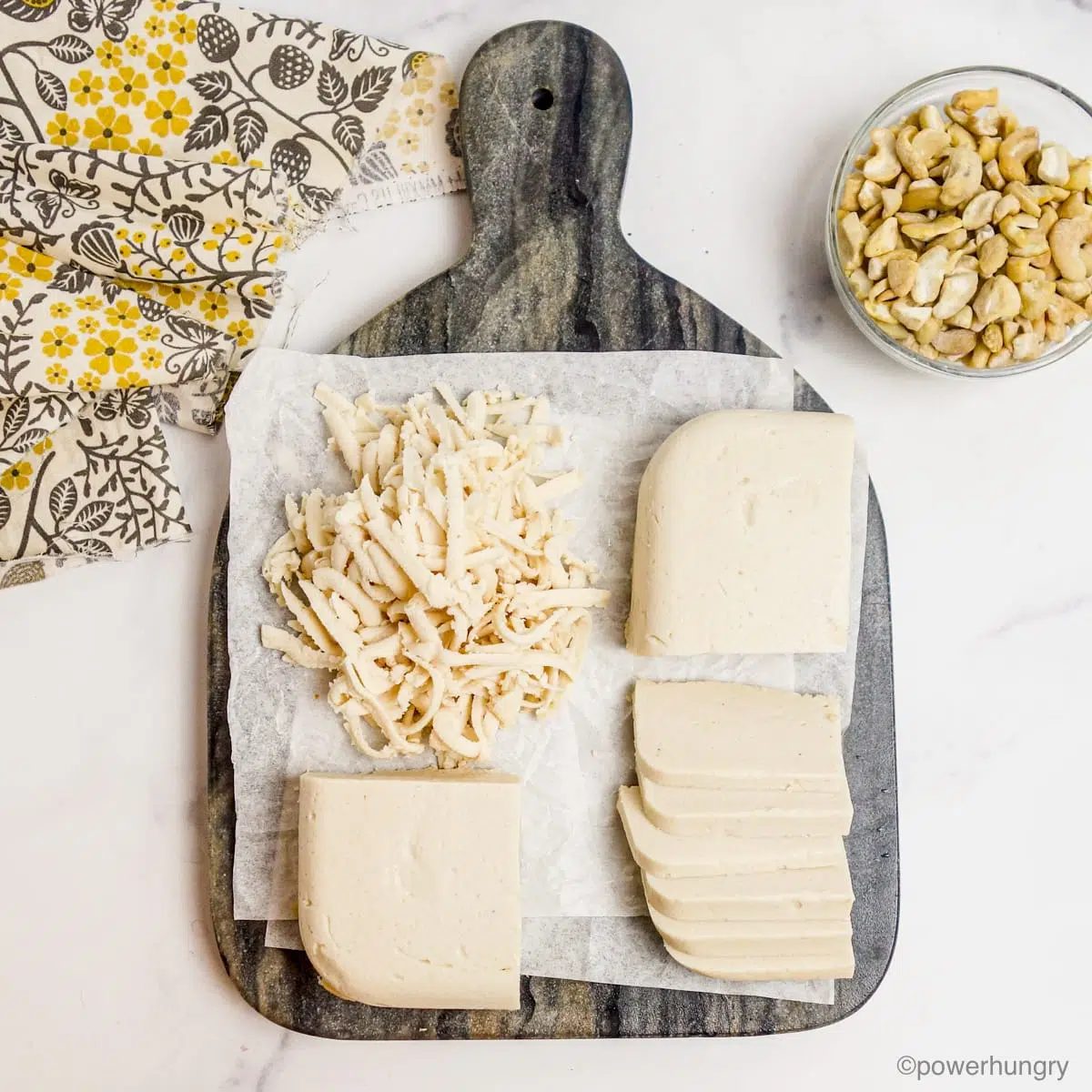 overhead of a tray of cashews, sliced vegan mozzarella, & grated mozzarella