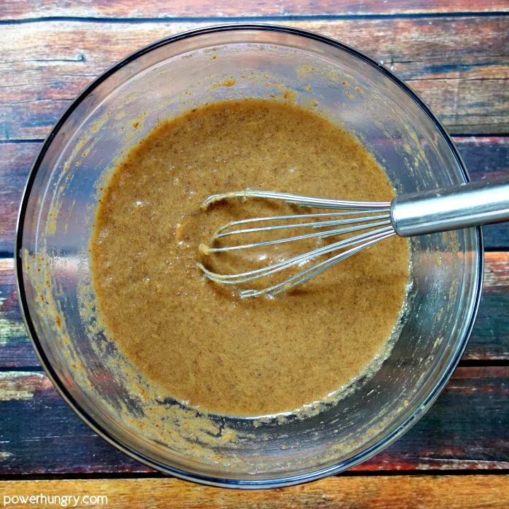 Liquid ingredients for peanut butter banana baked oatmeal cups in a glass mixing bow, with a whisk