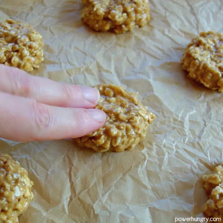 scooped cookie dough mounds being flattened on a baking sheet for oat protein cookies.