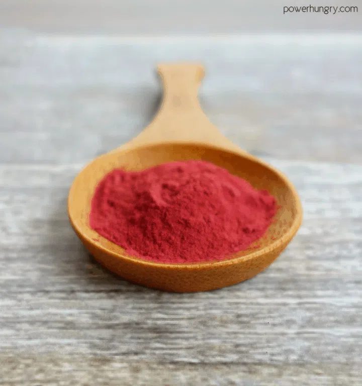 beet powder in a wooden spoon atop a wooden surface