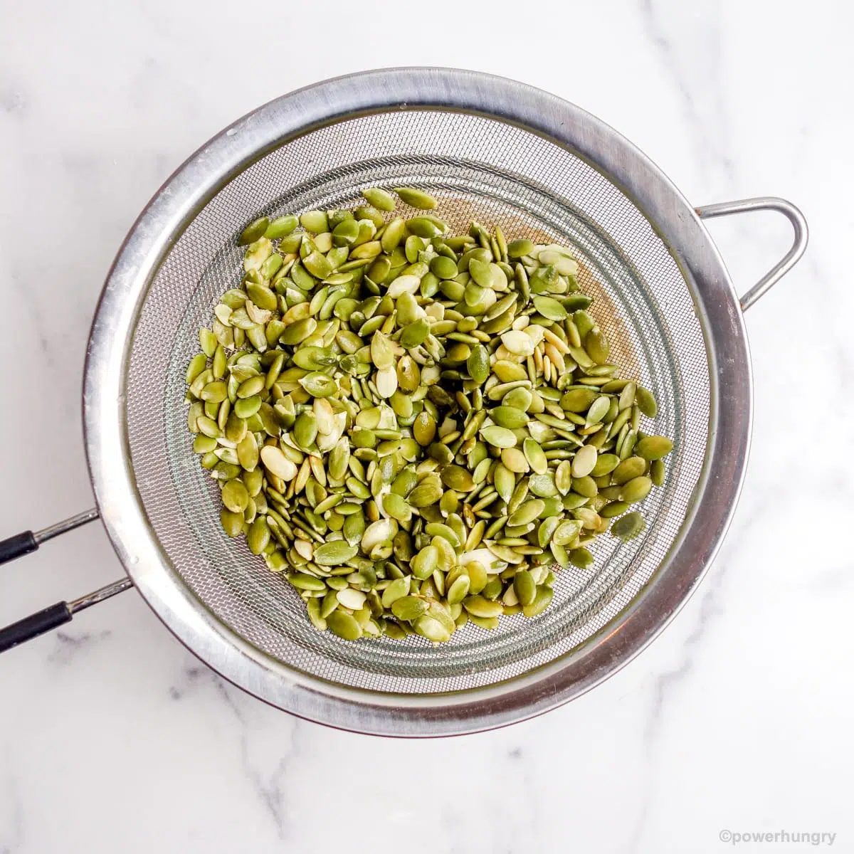 drained pumpkin seeds in a mesh colander over a glass bowl