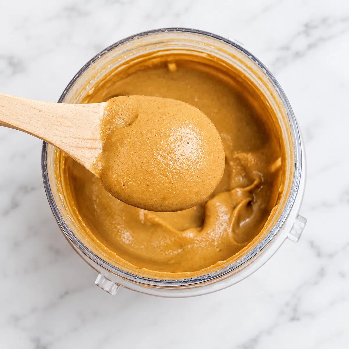 wooden spoon filled with roasted chickpea butter, from the jar seen below it