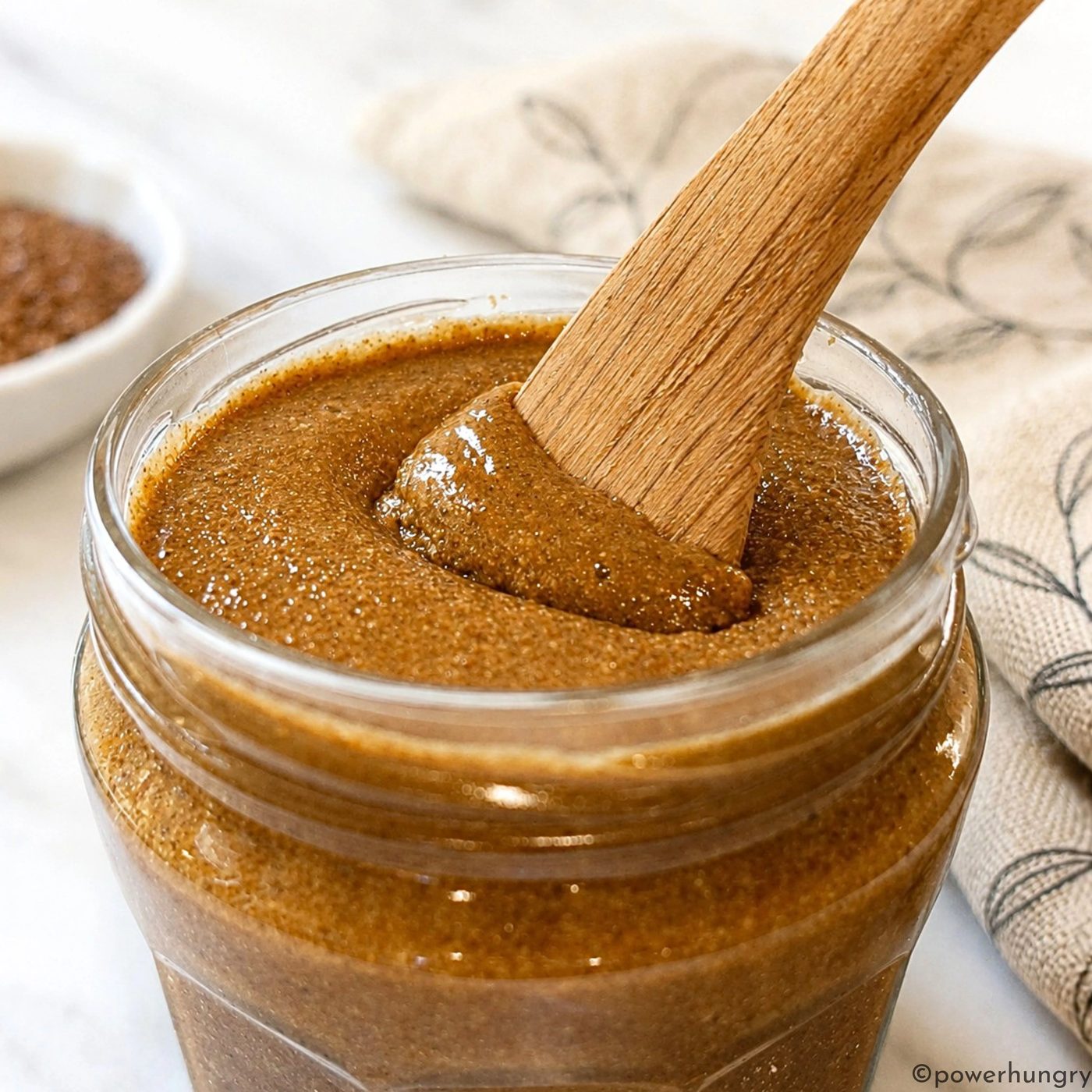 close-up of roasted flaxseed butter in a jar with a wooden spoon