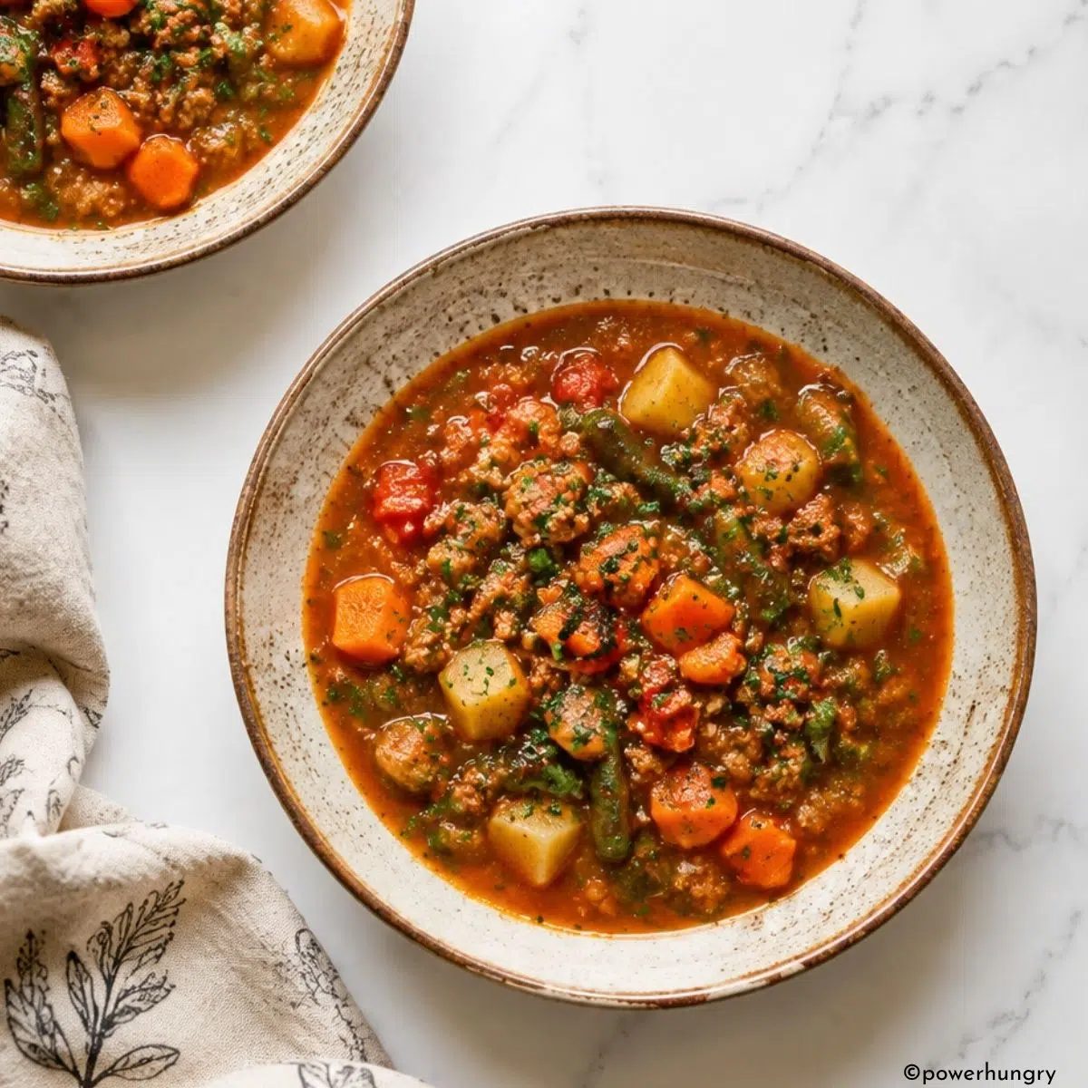 two bowls of crockpot vegan hamburger soup with a linen napkin alongside