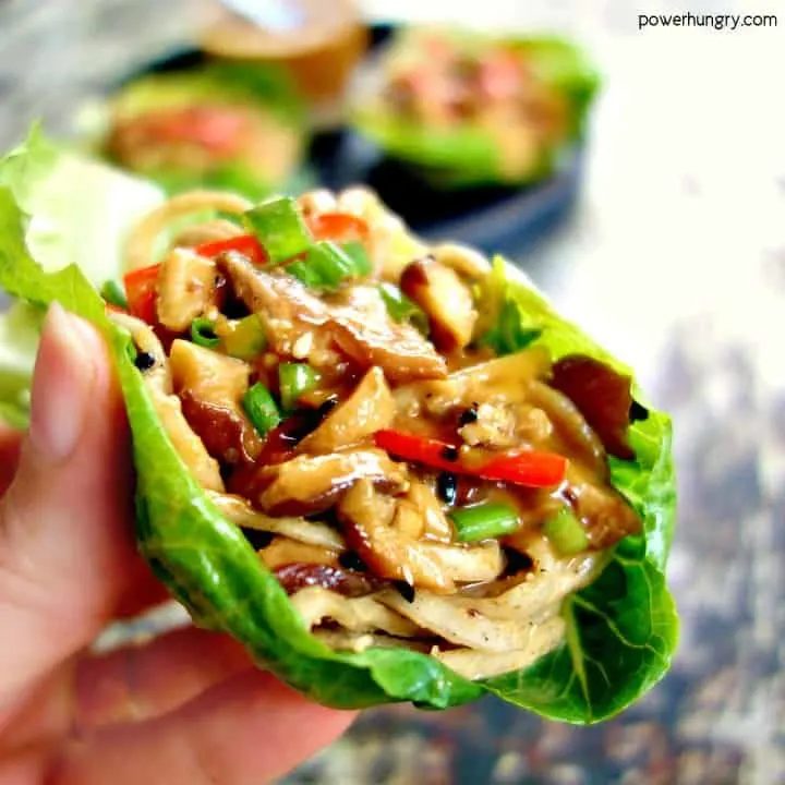 close-up of a hand holding a mushroom and soba noodle lettuce cup.