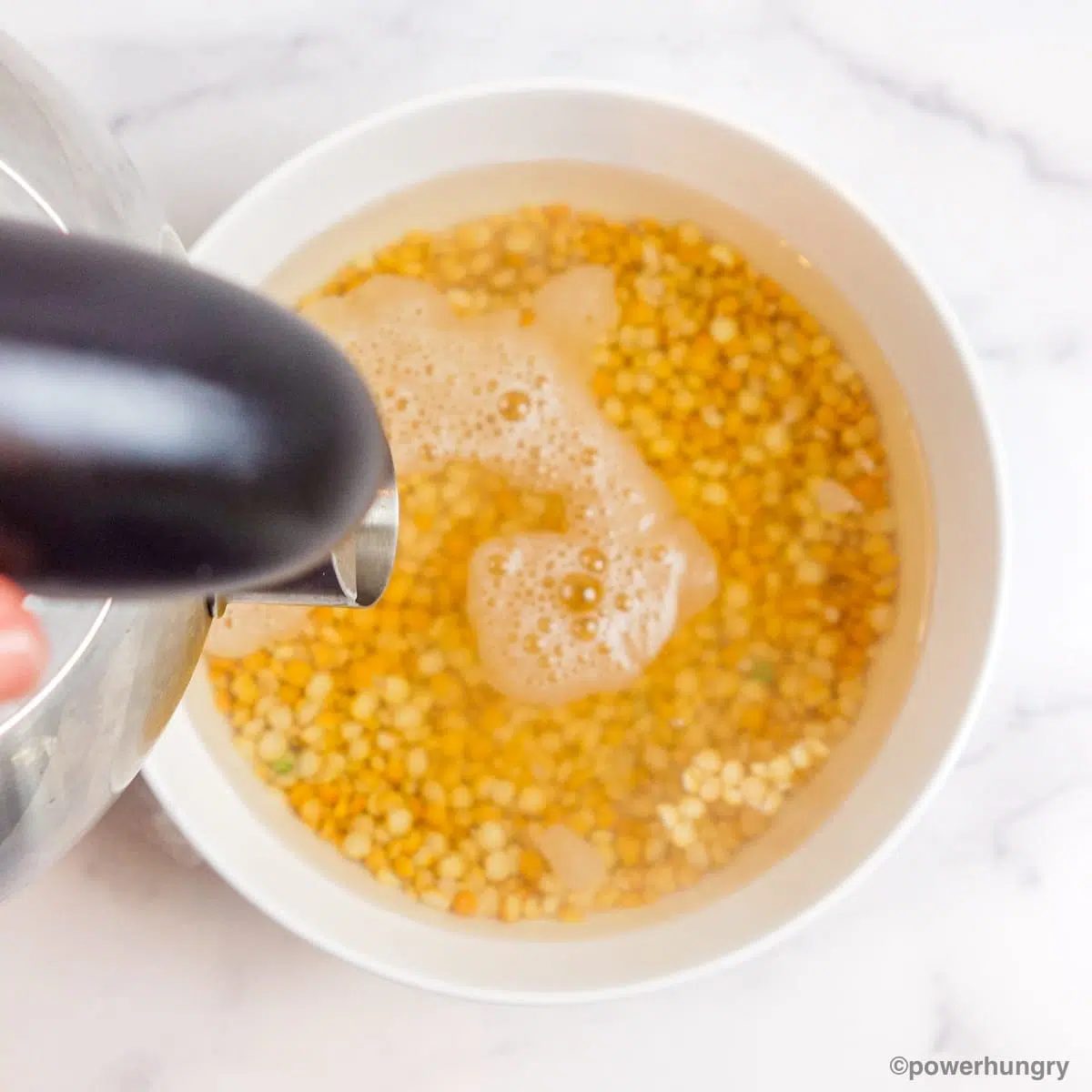yellow split peas in a white mixing bowl getting covered with boiling water