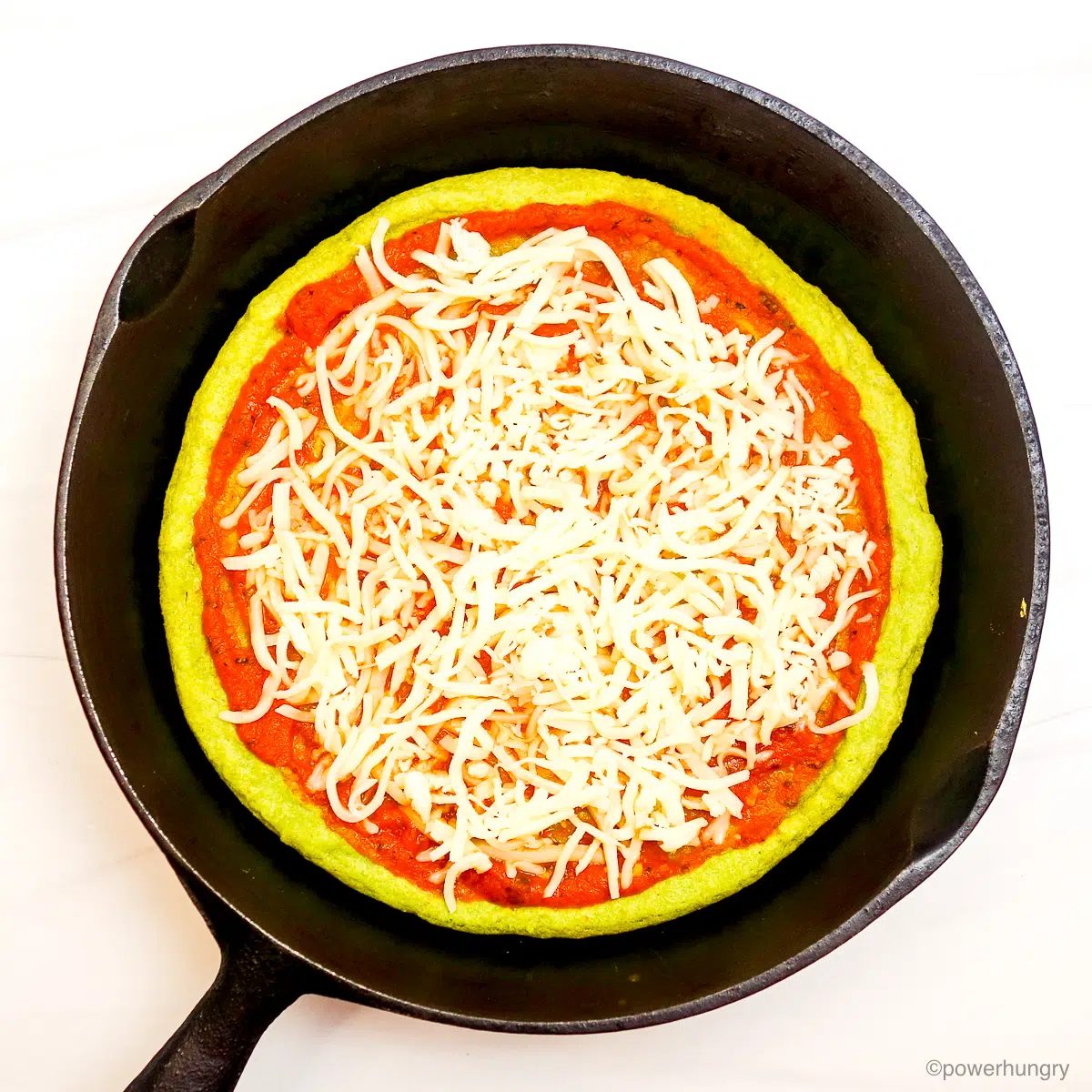 split pea pizza crust in skillet, topped with red sauce and mozzarella