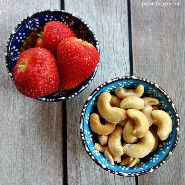 two small bowls, one filled with strawberries, the other, raw cashews