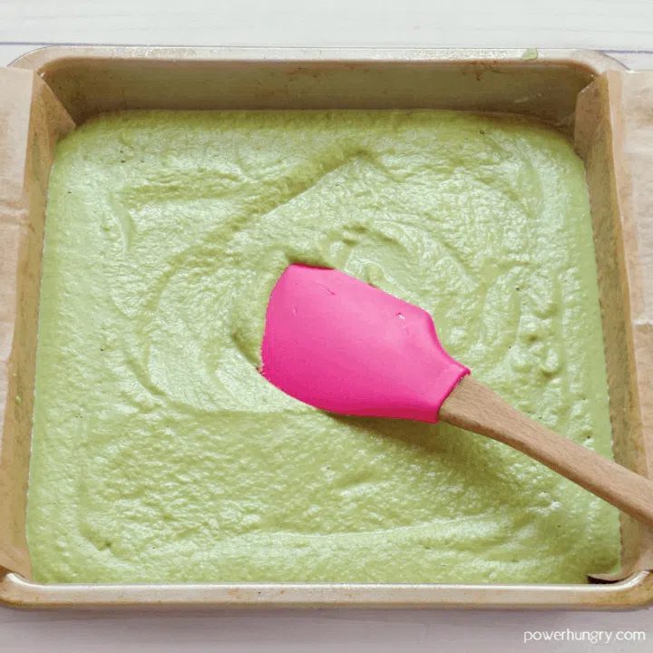 batter for herb lentil bread spread in a square pan with a pink spatula