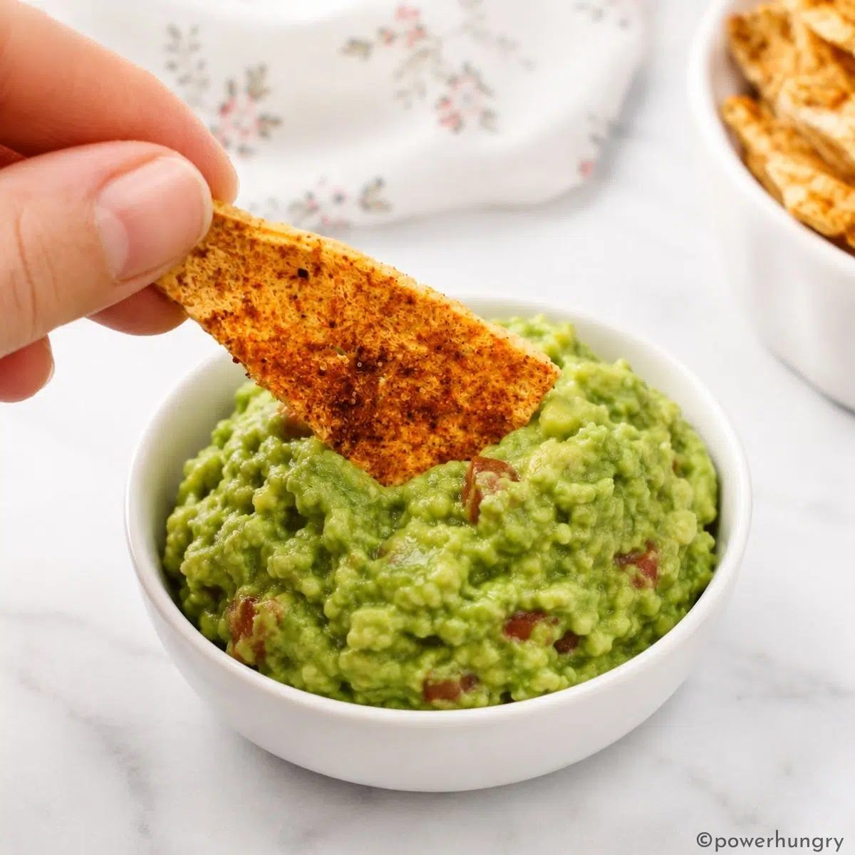 a single handheld tofu chip being dipped into guacamole