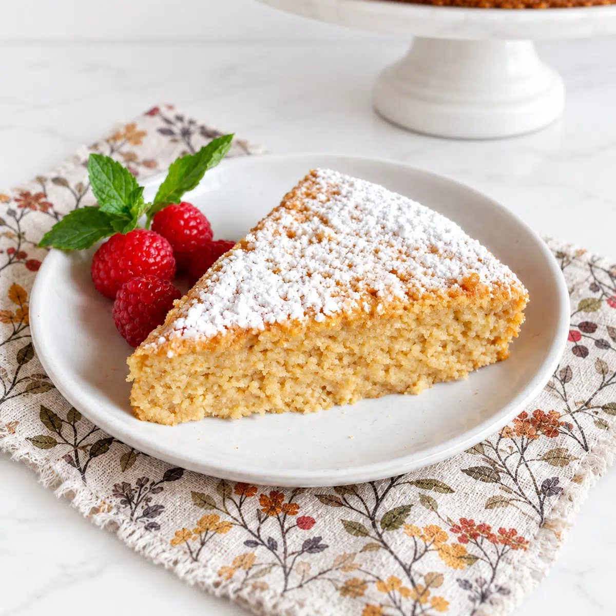 a slice of vegan almond flour cake on a white plate, with raspberries