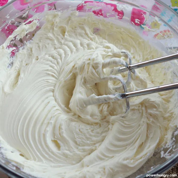 glass bowl filled with vegan vanilla frosting being beaten with electric beaters